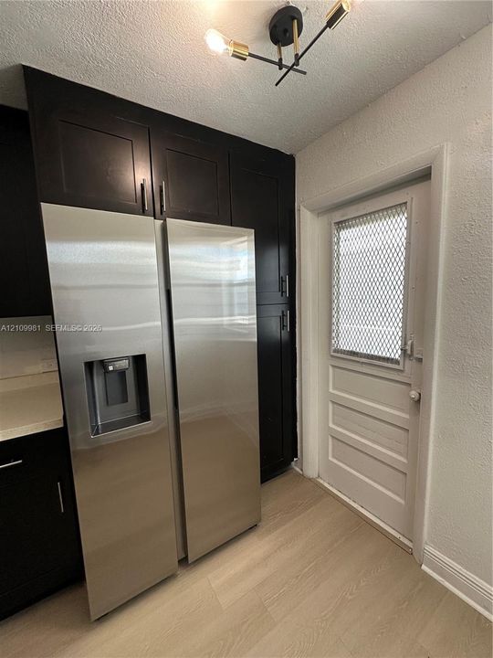 Dark cabinetry, stainless steel side-by-side refrigerator, wood-finish flooring, and multi-arm geometric ceiling fixture