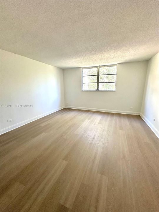 Neutral interior space featuring wood-finish flooring, white walls, and a multi-pane window