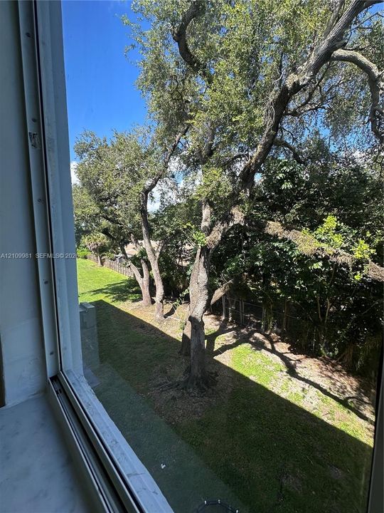 Exterior perspective featuring mature shade trees, established lawn, and metal fencing