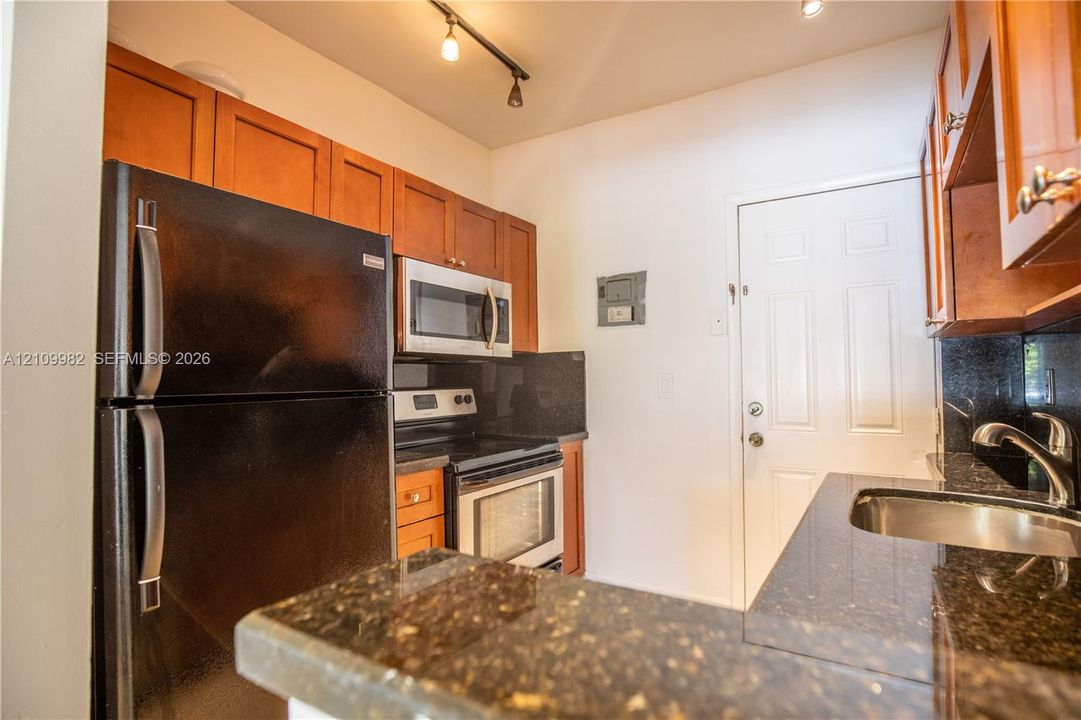 Kitchen featuring stained wood cabinetry, stone countertops, stainless steel appliances, and track lighting