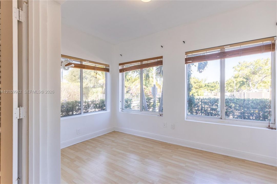 Light-filled room featuring wood-finish flooring, white walls, and multiple large windows with horizontal wood-slat blinds