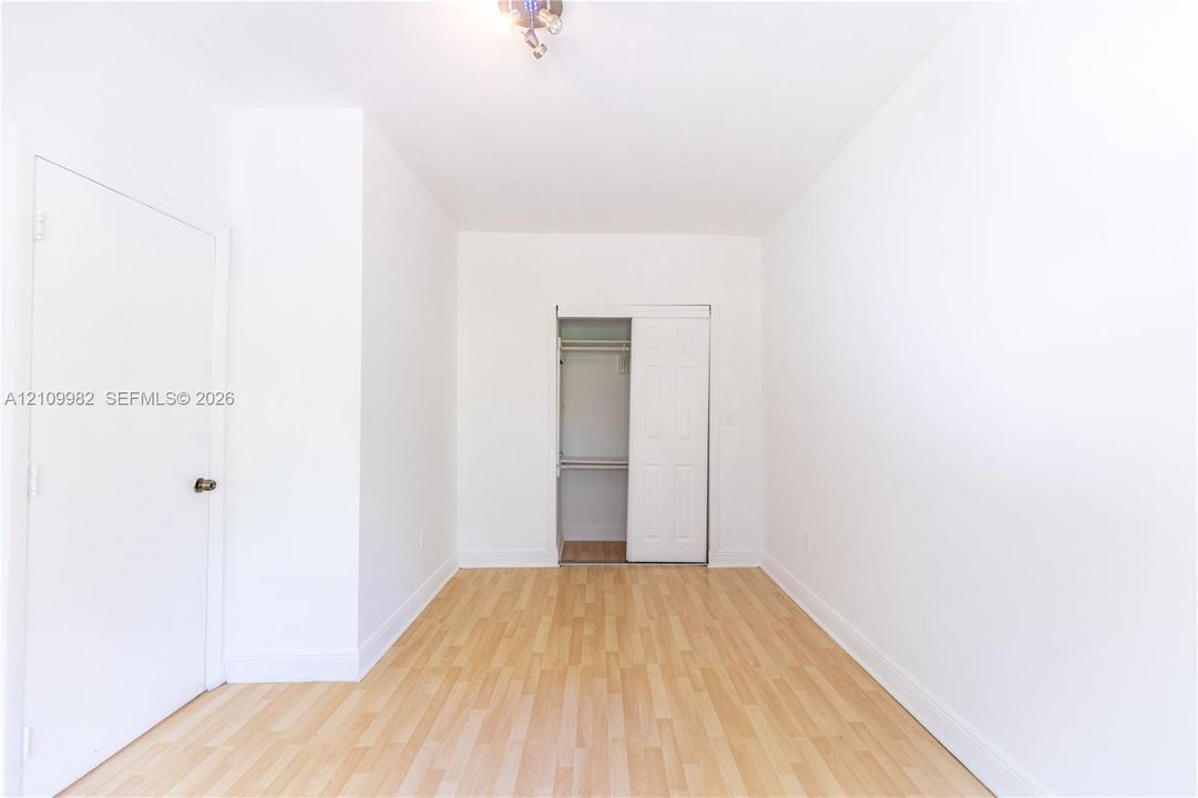Room featuring wood-finish flooring, white walls, a multi-panel door, and a built-in closet with sliding doors