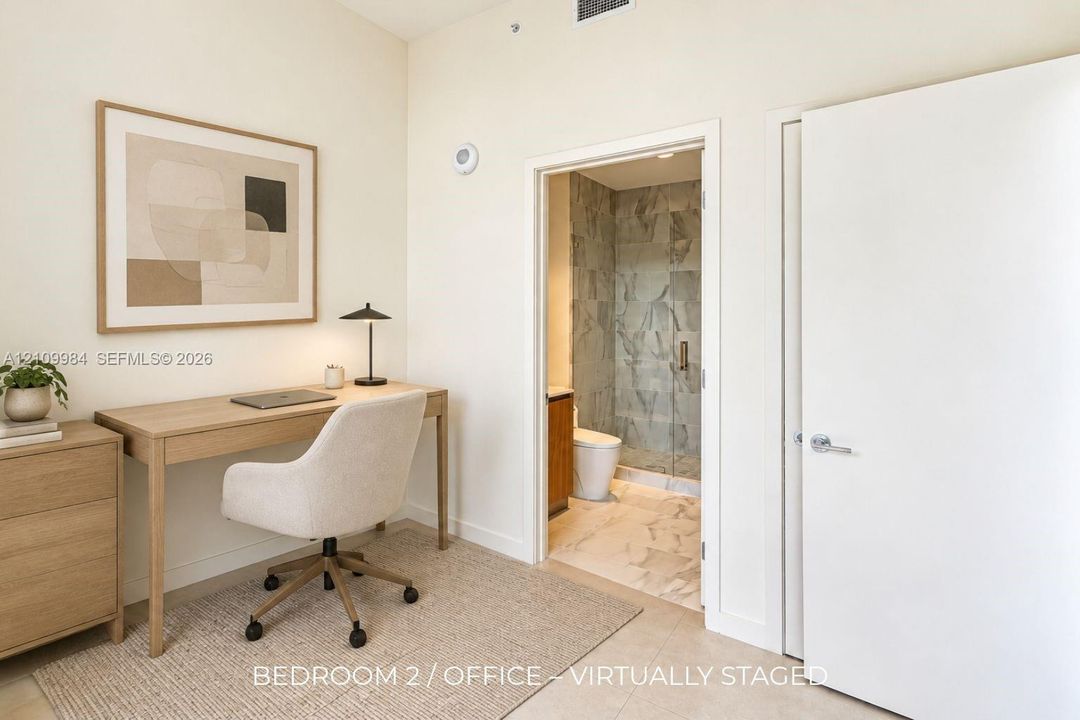 Neutral wall finishes with a full-height doorway opening to a bathroom featuring stone-patterned tile flooring, a glass-enclosed shower with large-format wall tile, and a wood-finish vanity cabinet