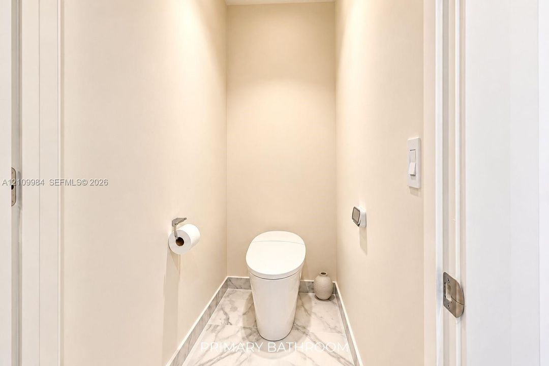 Enclosed water closet featuring a one-piece skirted toilet, large-format stone-finish floor tile, and brushed metal hardware