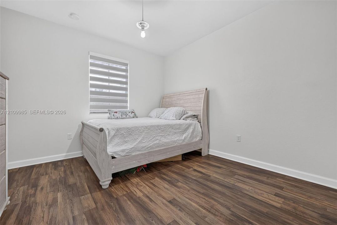 Interior room featuring wood-finish flooring, neutral wall paint, and a window equipped with dual-layered light-filtering shades
