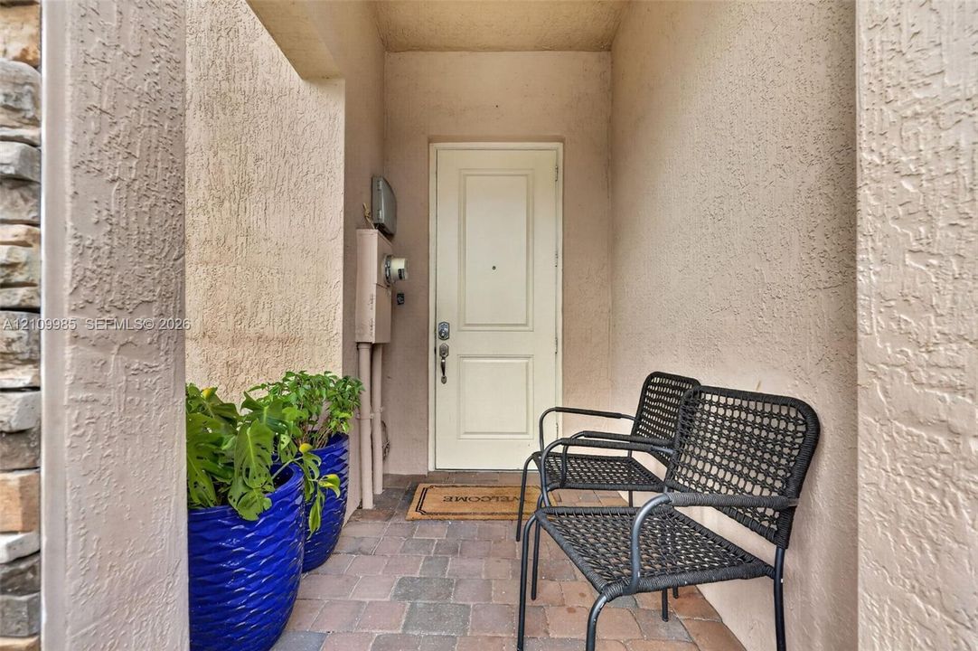 Covered entryway featuring a textured stucco facade, stone masonry accent, and paver flooring