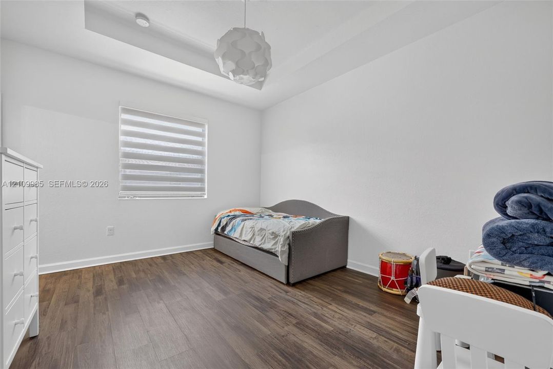 Tray ceiling featuring a contemporary geometric pendant light fixture, wood-finish flooring, and window with zebra-style shade
