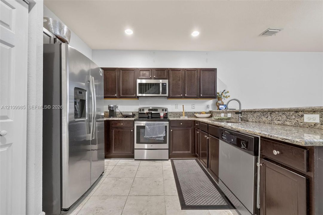 Kitchen featuring dark wood cabinetry, stone-finish countertops, stainless steel appliances, and ceramic tile flooring