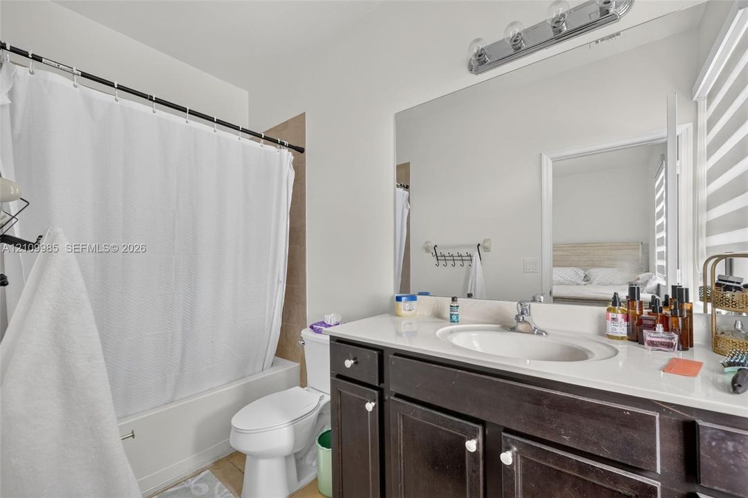 Bathroom featuring a vanity with dark-finish cabinetry, a solid-surface countertop with an integrated oval basin, a full-width vanity mirror, and a tub-shower combination with a tiled surround