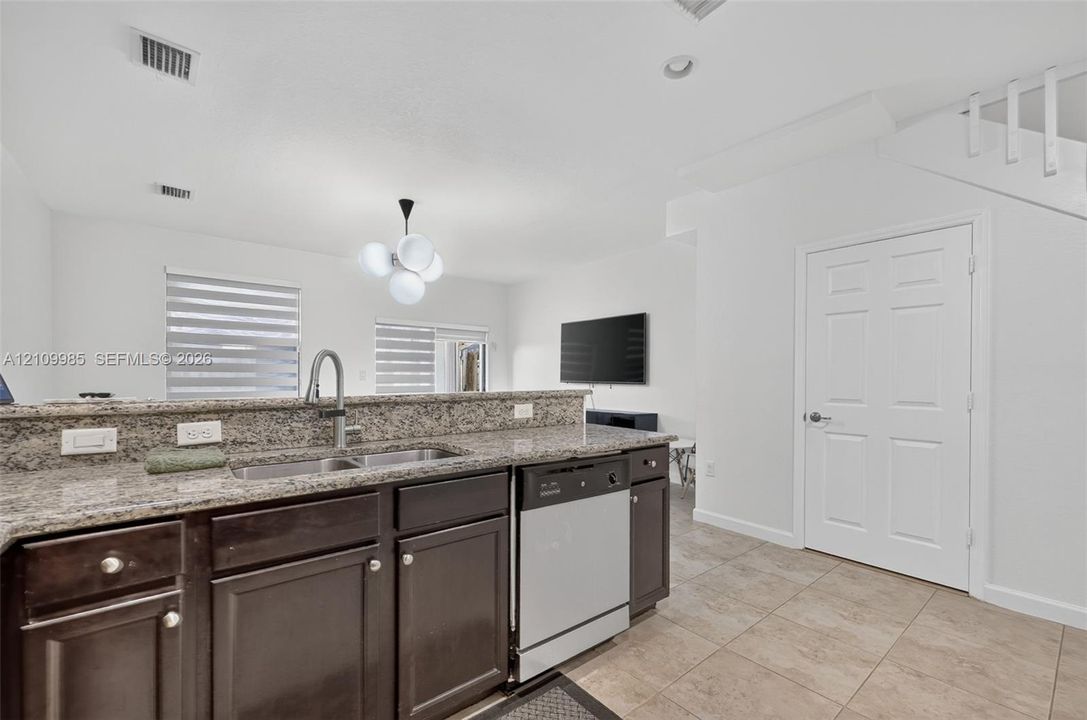 Kitchen featuring dark-finish cabinetry, stone-style countertops, an undermount dual-basin sink with a high-arch faucet, and stainless steel dishwasher