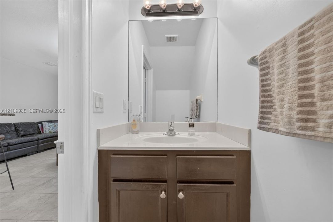 Vanity featuring a dark-finish wood cabinet, light-toned countertop with an integrated oval basin, polished metal hardware, a large wall-mounted mirror, and a four-bulb light fixture