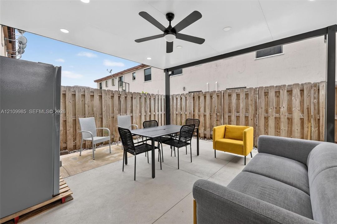Covered outdoor patio featuring a concrete floor, recessed lighting, and a ceiling fan, enclosed by a wood privacy fence