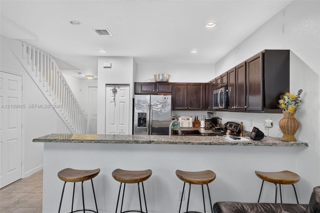 Kitchen featuring dark wood cabinetry, stone countertops, breakfast bar, recessed lighting, and stainless steel appliances