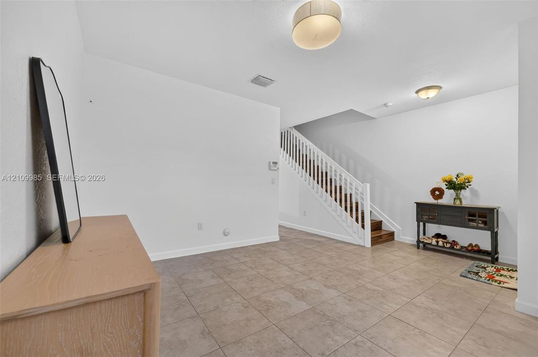 Open floor plan featuring neutral ceramic tile flooring, staircase with white wood balusters, and dual overhead drum light fixtures