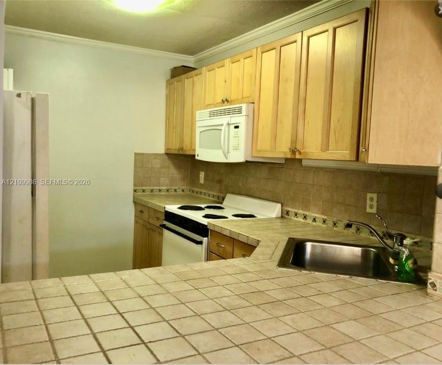 Kitchen featuring light-finish cabinetry, tiled countertops with a matching backsplash, a stainless steel sink with a goose-neck faucet, and white appliances
