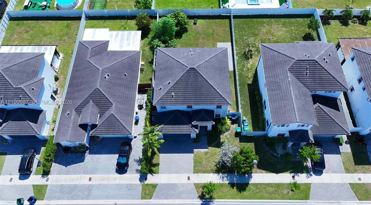 Aerial perspective of a two-story residence featuring a dark tile roof, smooth-stucco exterior, paver driveway, and a two-car garage