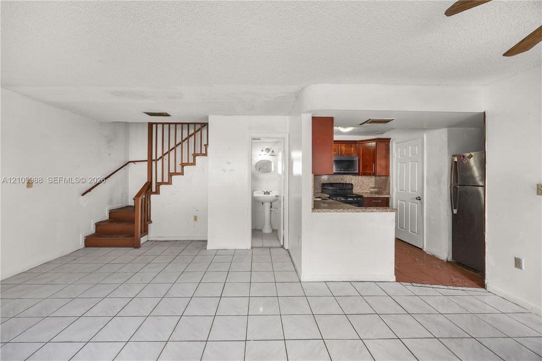Interior featuring white tile flooring, wooden staircase with matching handrail, kitchen with dark wood cabinetry and stone countertops, and a pedestal sink