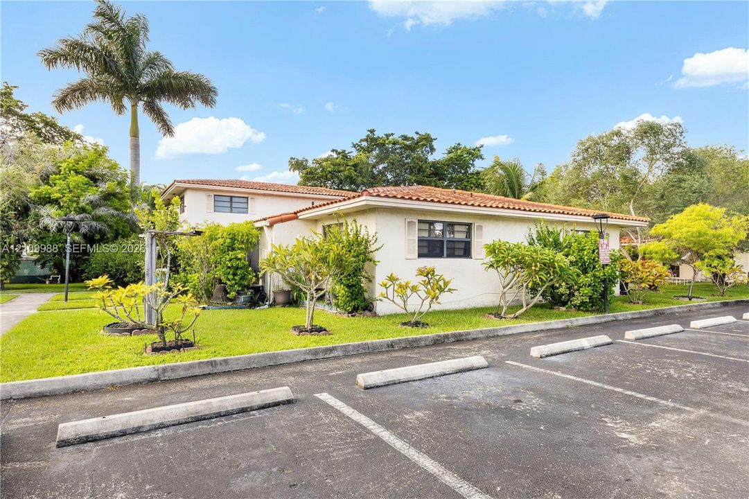 Stucco exterior featuring a terracotta tile roof, designated asphalt parking spaces, and established landscaping with mature palm trees
