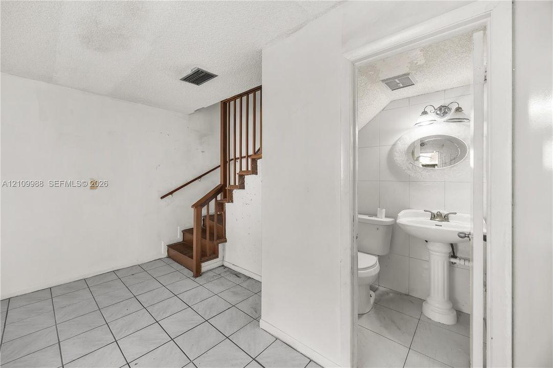 Staircase with wood railings and matching treads, tile flooring, pedestal sink, wall-mounted mirror, and wall-mounted light fixture