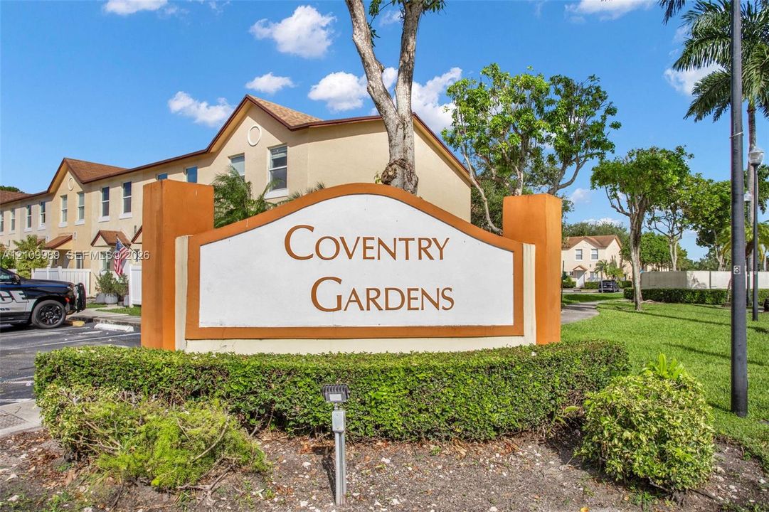 Community monument sign featuring stucco and stone-finish pillars, complemented by manicured shrubbery and mature landscaping