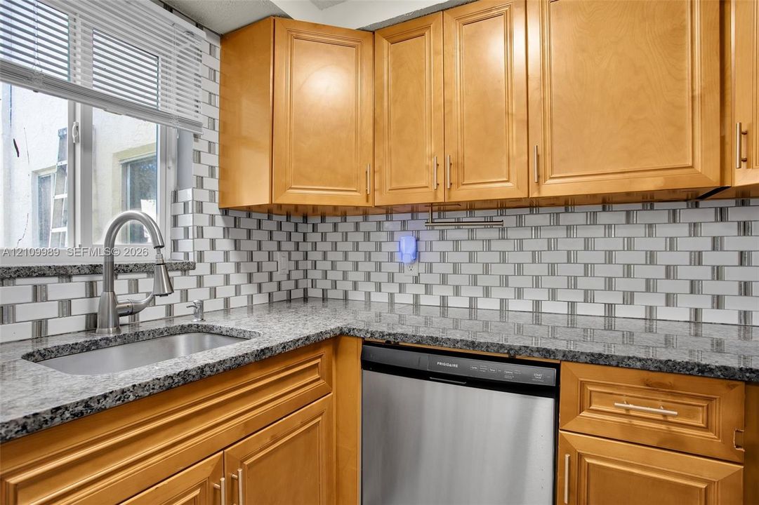 Kitchen featuring honey-tone cabinetry, stone-finish countertops, subway tile backsplash, stainless steel dishwasher, and undermount sink with a gooseneck faucet