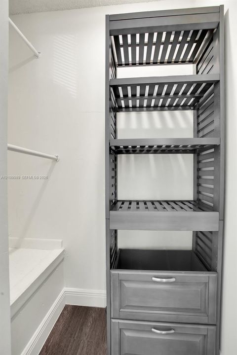 Built-in gray cabinetry featuring slatted open shelving and two lower drawers with metallic hardware, complemented by white structural shelving rods and wood-finish flooring