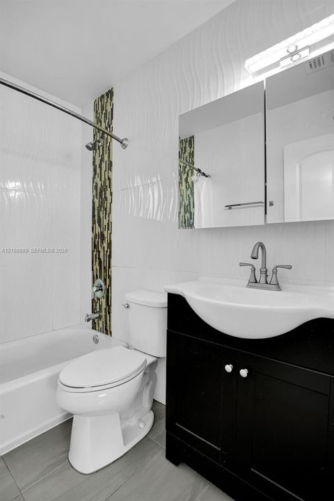 Bathroom featuring a dark wood-finish vanity, integrated sink, vertical mosaic tile accent, textured wall tile, and gray floor tiling