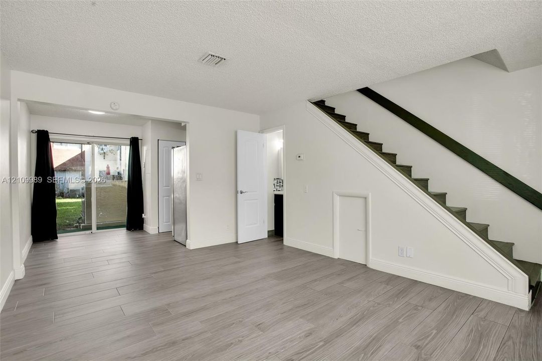 Open interior space featuring wood-finish flooring, staircase with a handrail, sliding glass door, and recessed storage area