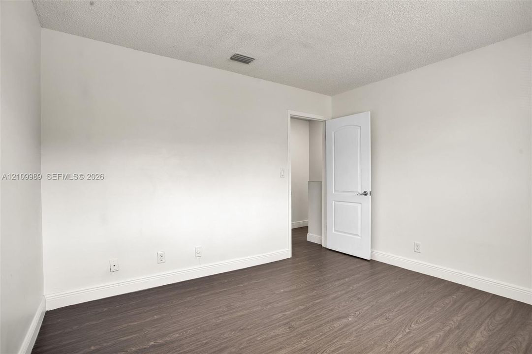 Interior room featuring wood-finish flooring, white walls, and a two-panel interior door with a metallic lever handle