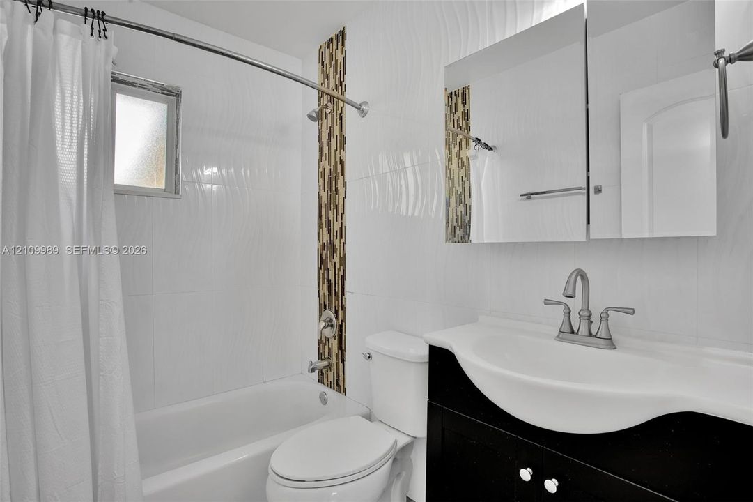 Bathroom featuring white textured wall tile, a vertical stone-mosaic accent band, a black vanity with a molded basin, and a mirrored medicine cabinet