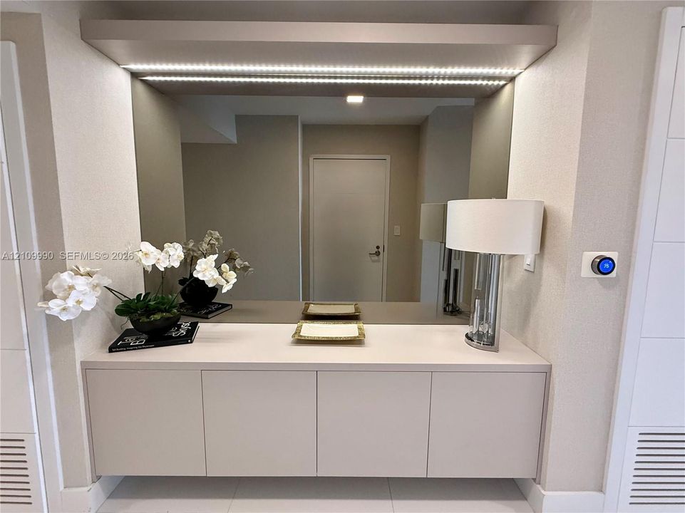 Built-in floating cabinetry featuring a solid surface countertop, expansive wall-to-wall mirror, and integrated LED accent lighting