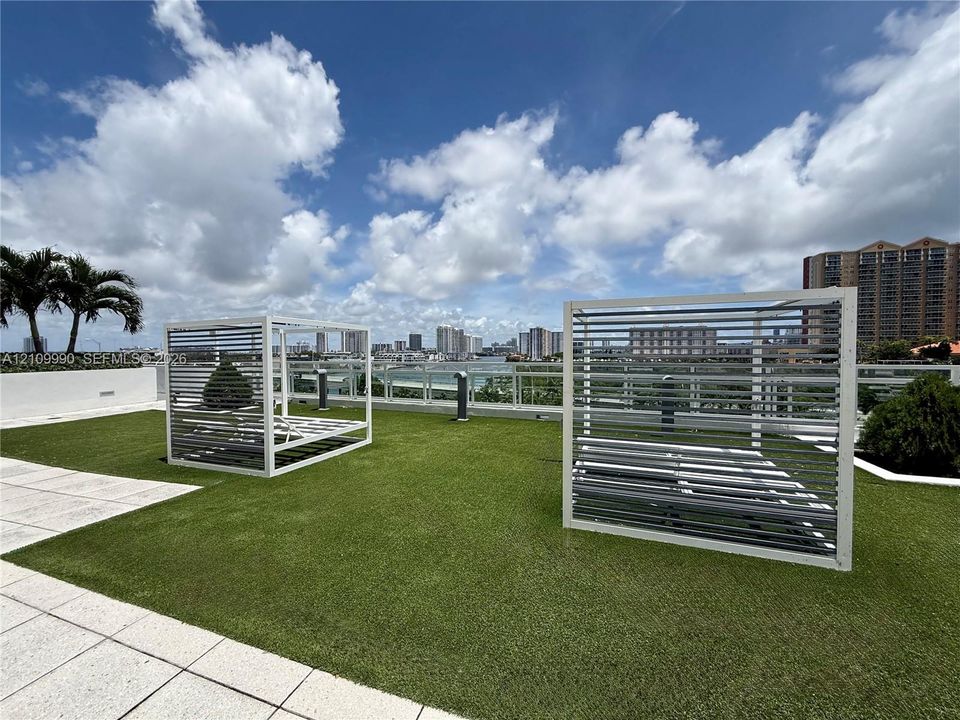 Rooftop terrace featuring synthetic turf, glass panel railings, and white metal louvered privacy structures