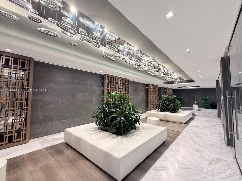 Lobby featuring stone tile flooring, geometric wood wall screens, expansive linear ceiling lighting, and built-in rectangular planters