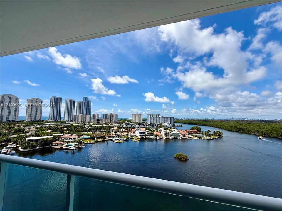 Covered balcony featuring a glass panel railing and panoramic waterway and urban skyline scenery