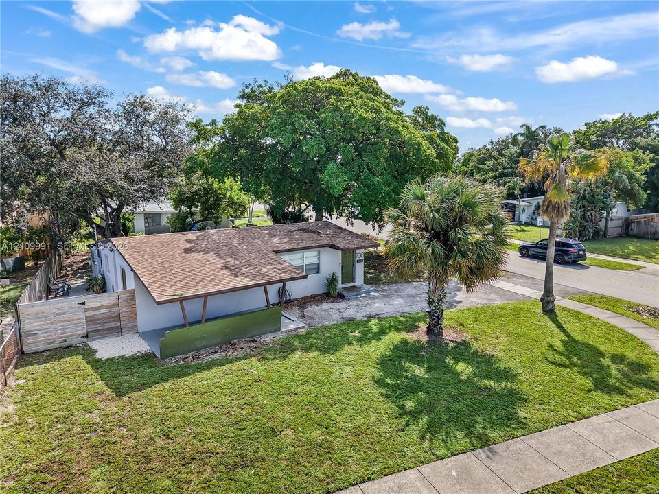 Single-story exterior featuring a shingled roof, overhanging carport, integrated wood-finish fencing, and established palm and shade trees