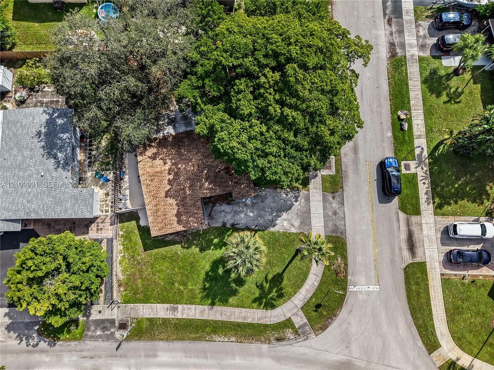 Aerial perspective of corner lot featuring a paved driveway, mature shade trees, and established lawn landscaping