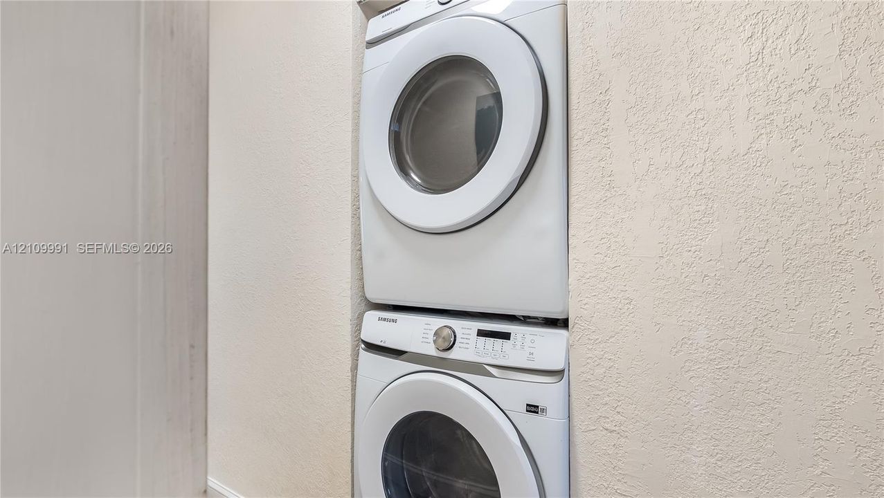 Stacked white washer and dryer unit housed within a recessed wall cavity