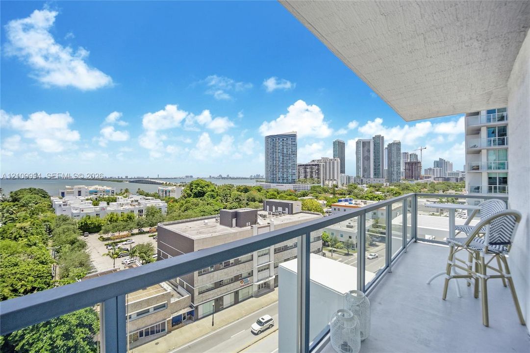 Private balcony featuring a glass-panel railing and concrete flooring, overlooking an expansive cityscape and coastal horizon