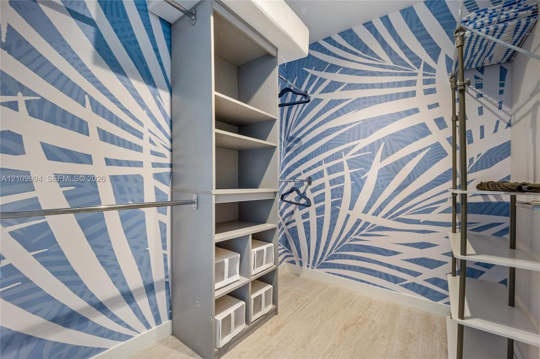 Walk-in closet featuring custom built-in shelving, vertical storage compartments, metallic hanging rods, and patterned wall covering