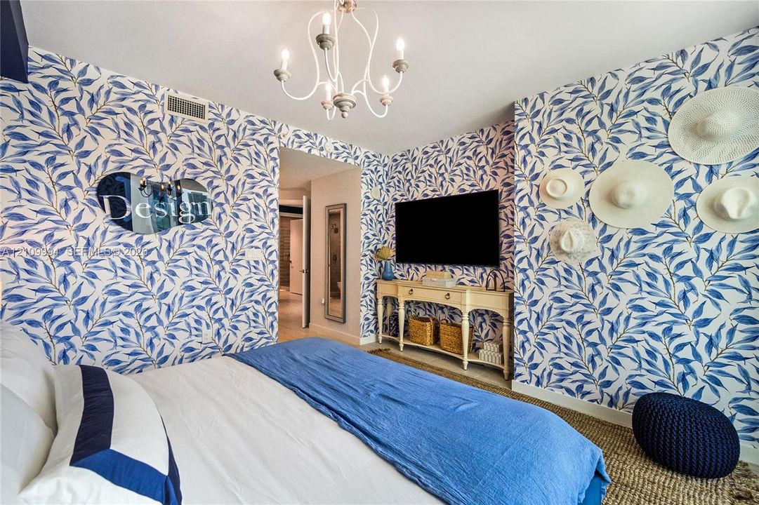 Interior space featuring patterned botanical wallpaper, a multi-arm white chandelier, and woven floor covering