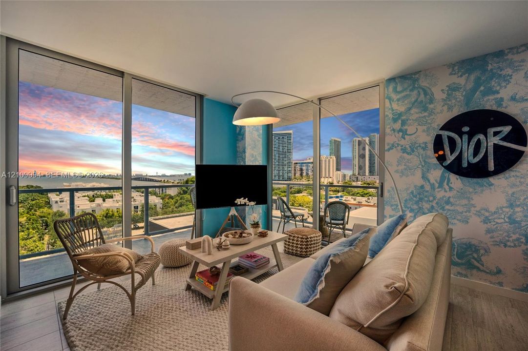 Floor-to-ceiling glass walls, integrated balcony access, wood-finish flooring, and expansive exterior water and urban scenery