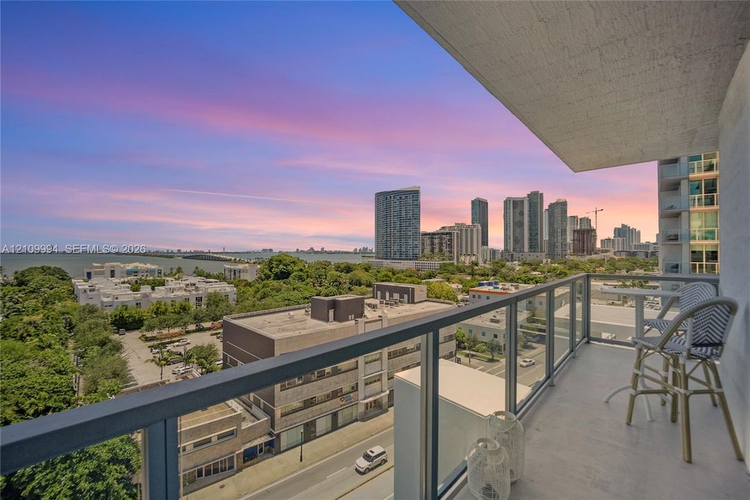 Covered balcony with a metal-framed glass railing and concrete flooring overlooking the urban skyline and water