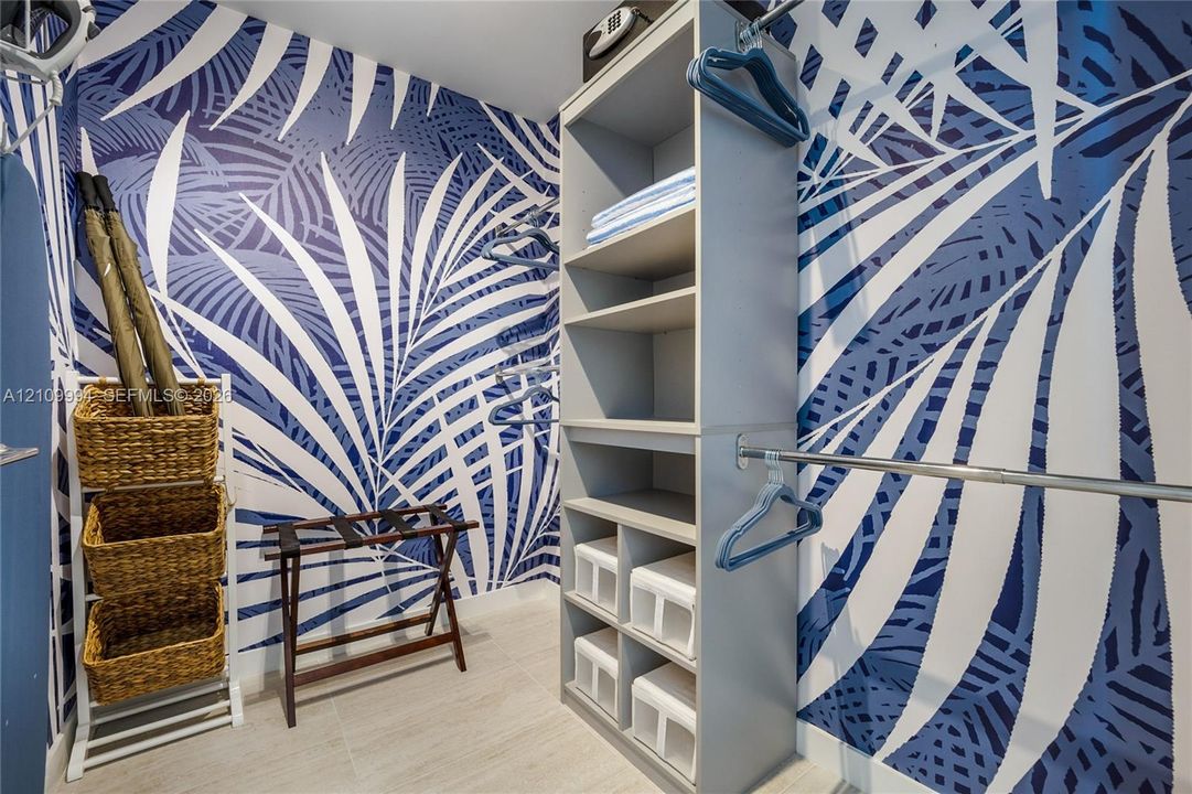 Walk-in closet featuring built-in gray laminate shelving, hanging rods, and patterned wallpaper