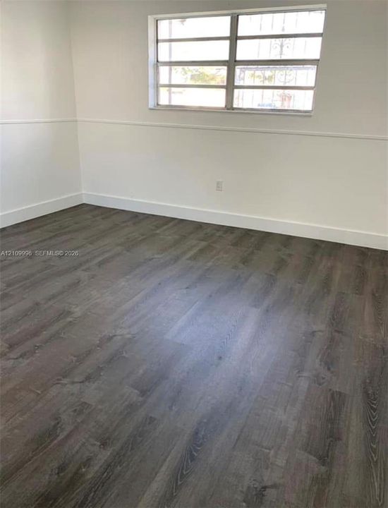 Interior space featuring wood-finish flooring, white walls with chair rail molding, and a multi-pane horizontal window
