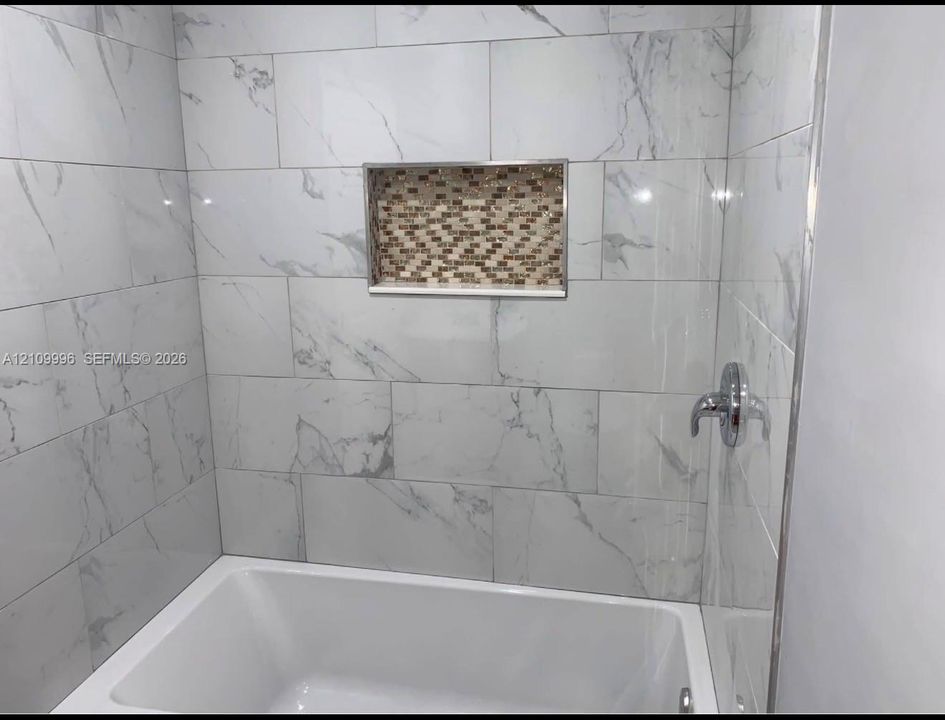 Bathtub shower combination featuring large-format stone-patterned wall tiles, a recessed tile-accented niche, and polished chrome plumbing fixtures