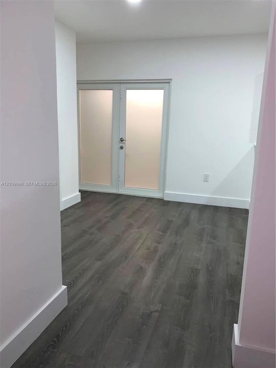 Room featuring wood-finish flooring, white walls, and double French doors with frosted glass panels