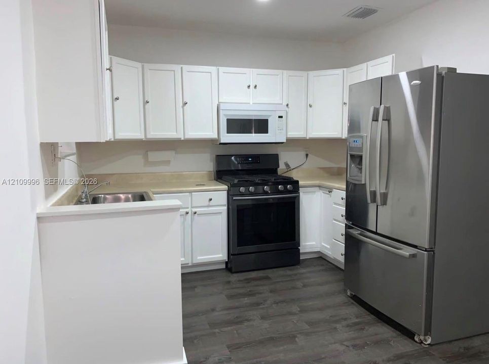 Kitchen featuring white cabinetry, wood-finish flooring, a stainless steel refrigerator, a built-in microwave, and a black gas range