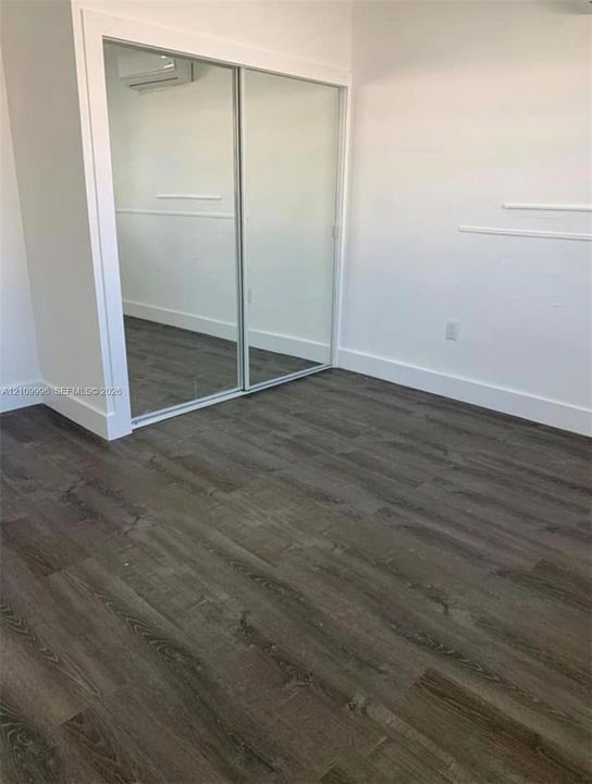 Wood-finish flooring, sliding mirrored closet doors, and wall-mounted climate control unit
