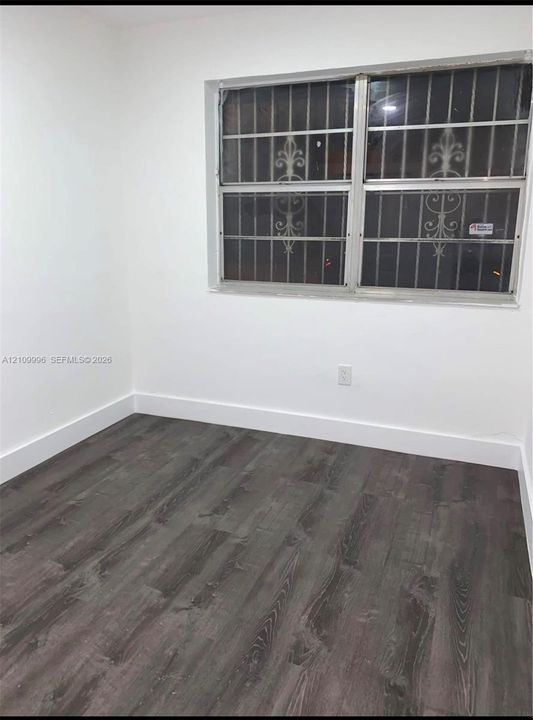 Neutral-toned wood-finish flooring and bright white walls featuring a window with integrated decorative metal security bars