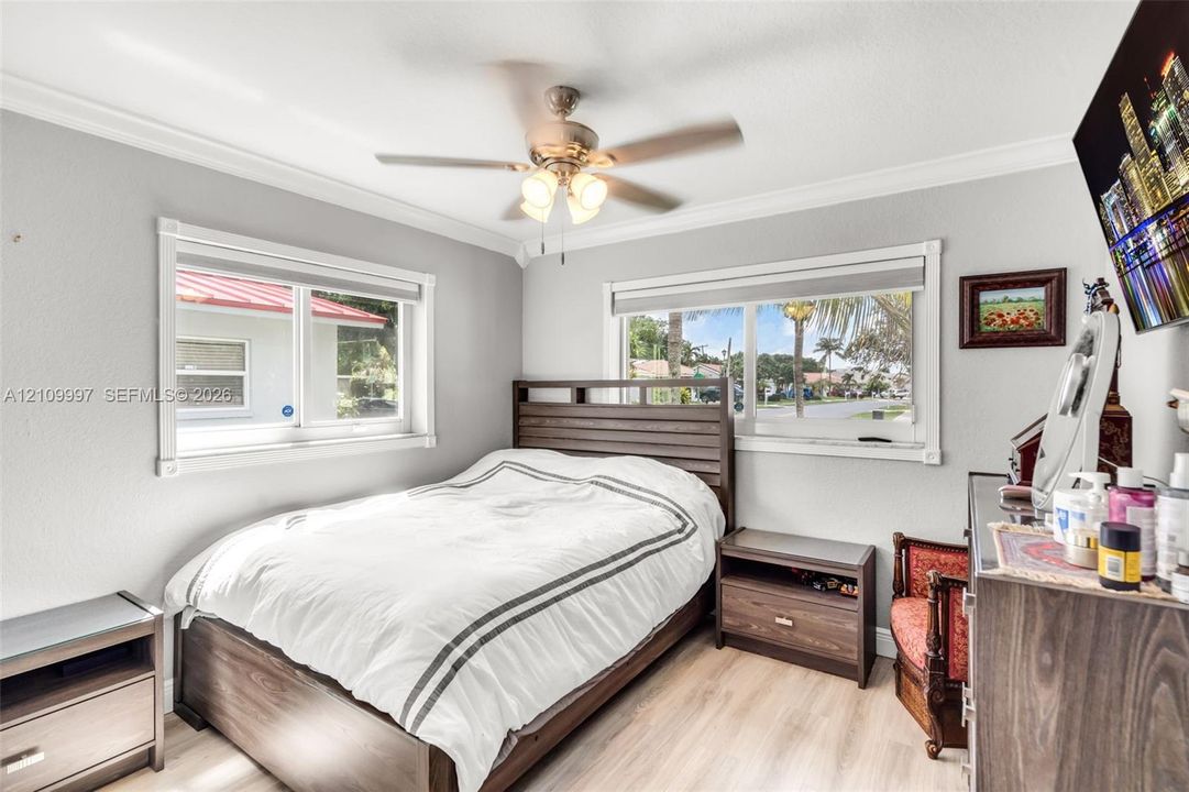 Neutral-toned interior featuring wood-finish flooring, dual windows, crown molding, and a central ceiling fan with integrated lighting